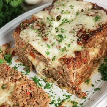 Meatloaf topped with melted cheese and fresh herbs on a platter.