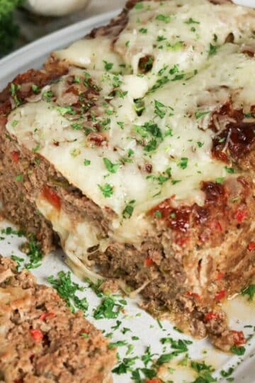 Meatloaf topped with melted cheese and fresh herbs on a platter.