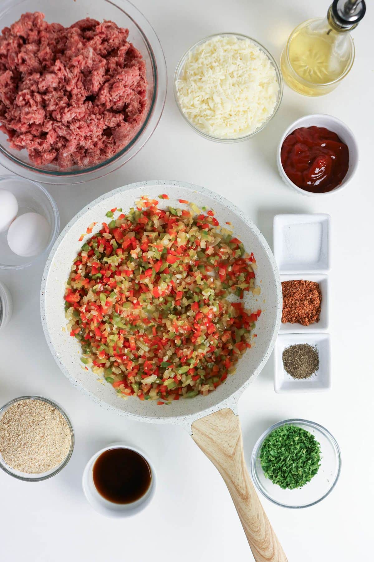 A skillet of sautéed peppers surrounded by bowls of ground meat, cheese, seasonings, and other ingredients.